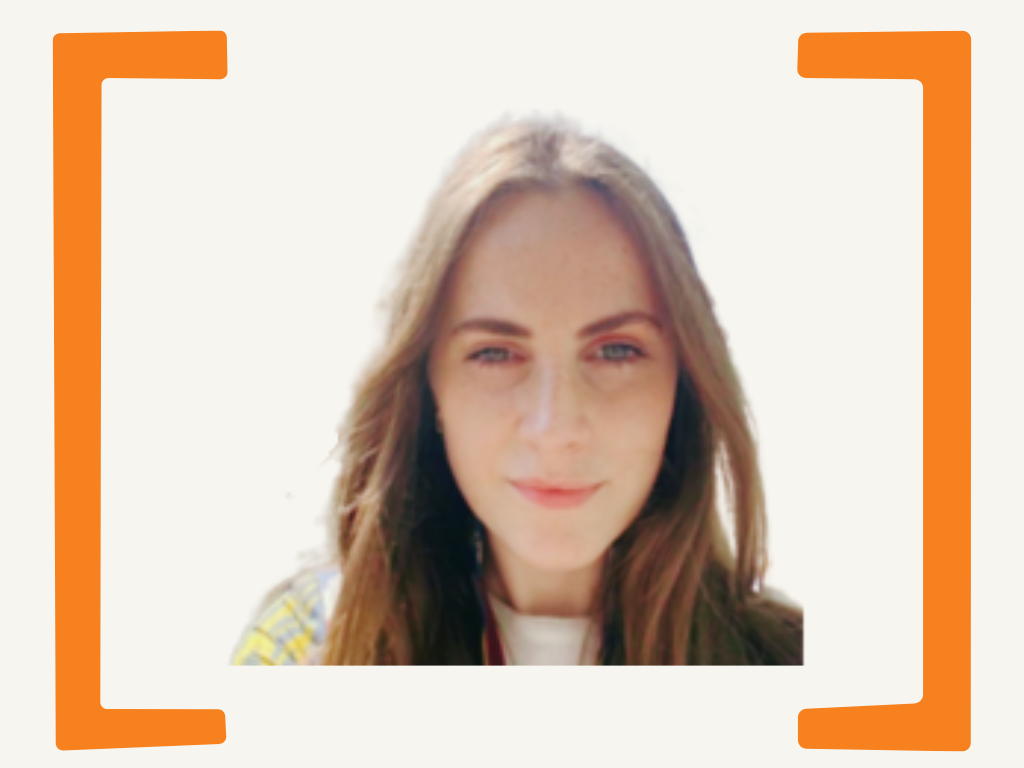 Close-up of a young woman with long brown hair, fair skin, and blue eyes, smiling slightly against a bright background with orange border frames.